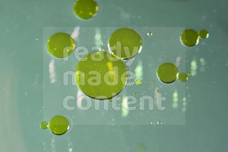 Close-ups of abstract yellow watercolor drops on oil Surface on green background