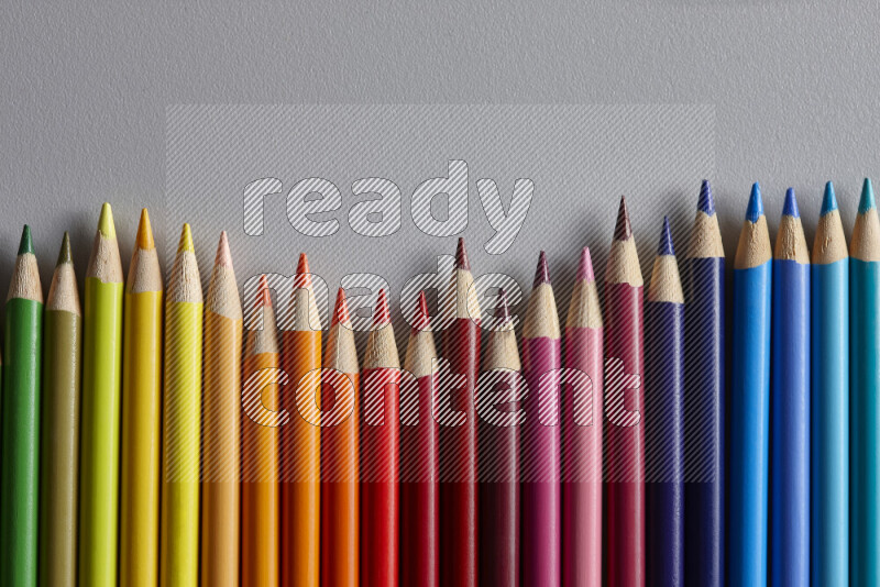 A collection of colored pencils arranged showcasing a gradient of different hues on grey background