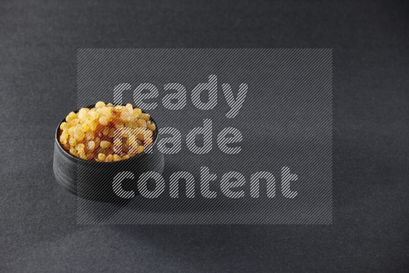 وعاء فخاري أسود ممتلئ بالزبيب الأصفر على خلفية سوداء