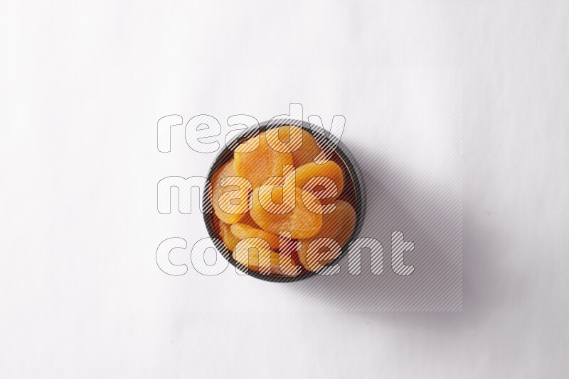 Dried apricots in a black pottery bowl on white background