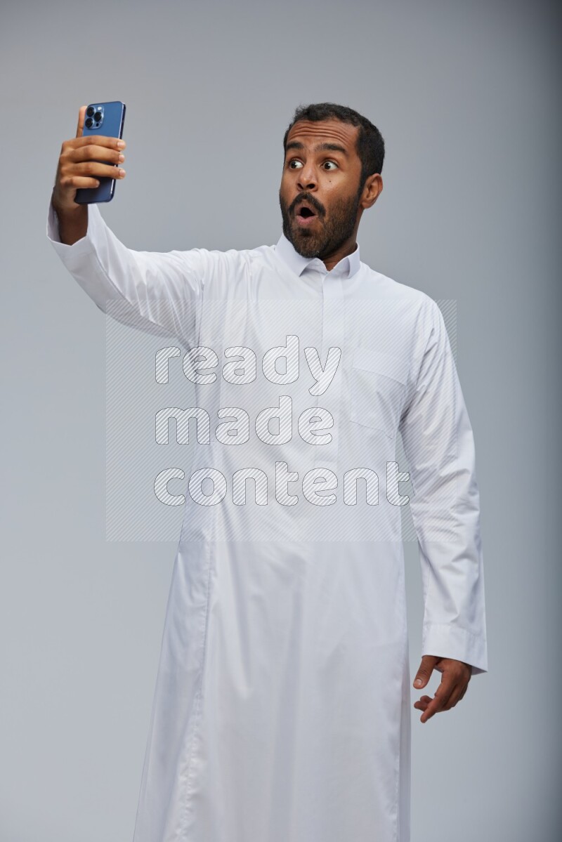 Saudi man wearing Thob standing taking selfie on Gray background