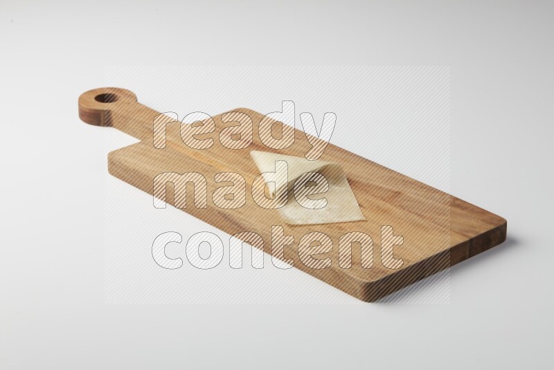 One uncooked samosa on a wooden cutter on a white background