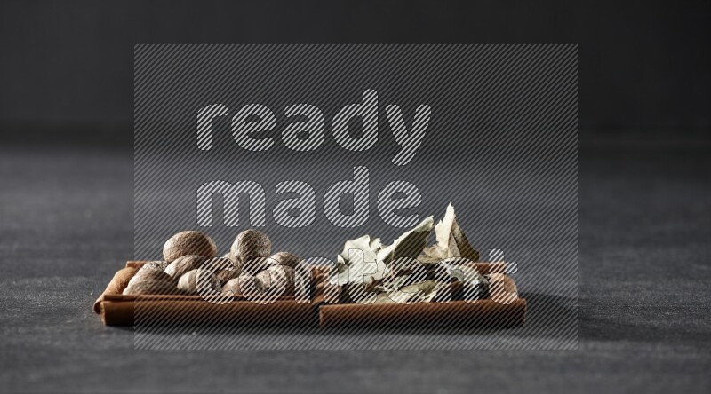 مربعان من أعواد القرفة ممتلئان بجوزة الطيب وأوراق الغار علي خلفية سوداء