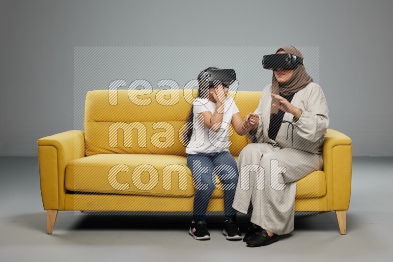 A girl and her mother sitting playing with VR on gray background