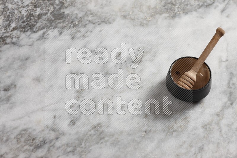 Black pottery bowl with wooden honey dipper in it on grey marble background