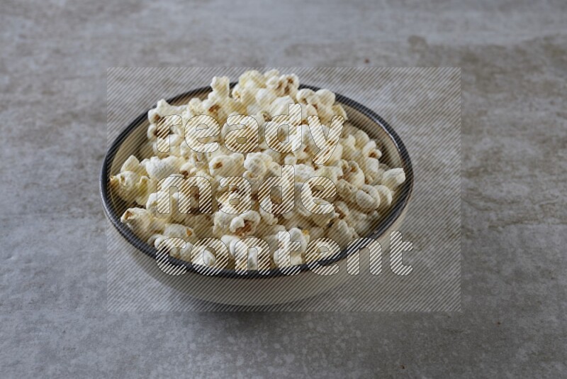 popcorn in a multi-colored pottery bowl on a grey textured countertop