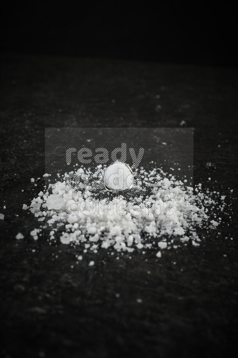 2 metal spoons filled with white salt on black background