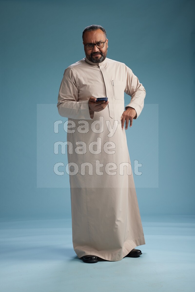 Saudi Man without shimag Standing texting on phone on blue background