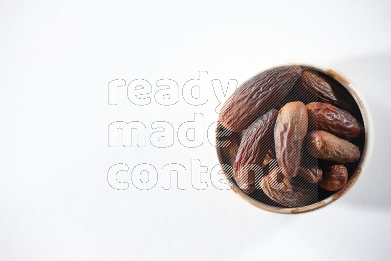 A beige ceramic bowl full of dried dates on a white background in different angles