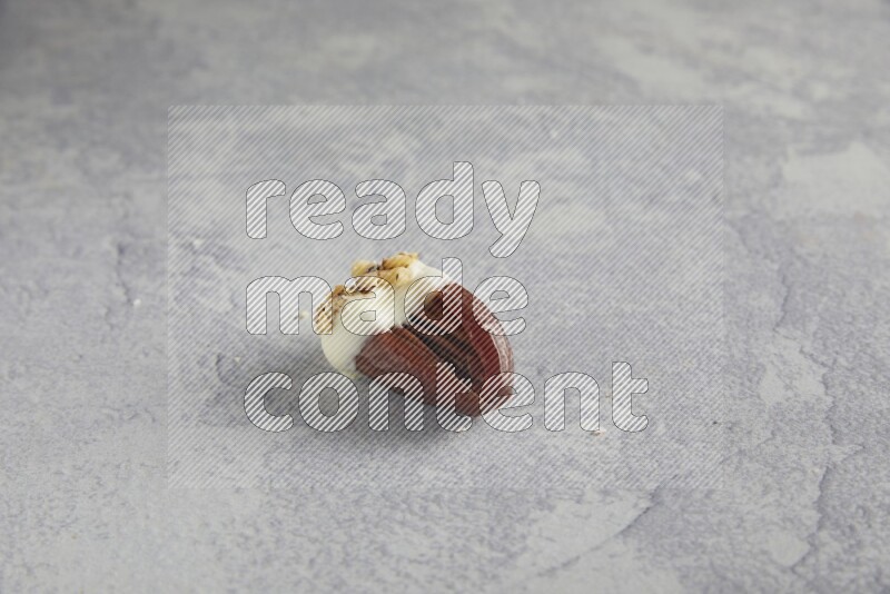 Pecan stuffed date covered with white chocolate and chopped walnuts on alight grey background