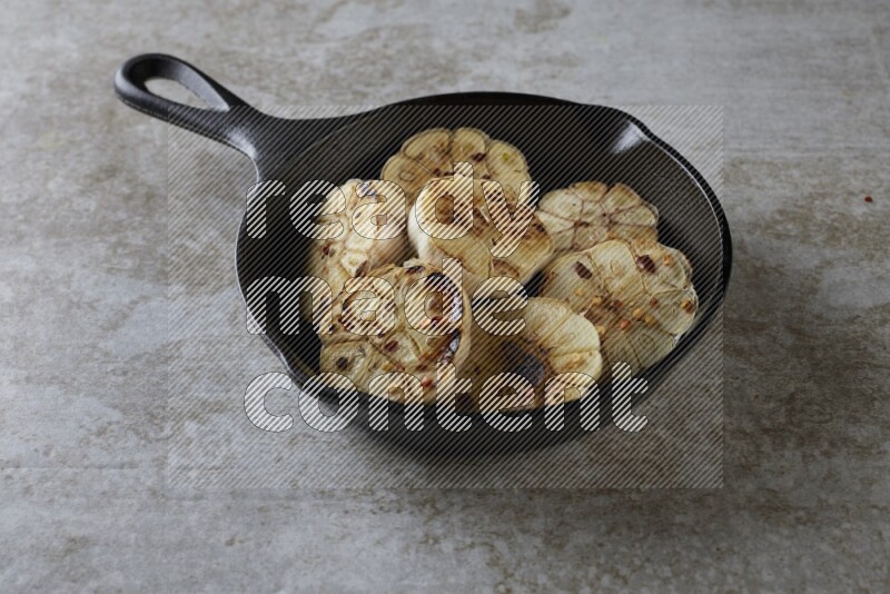half's roasted garlic in a black pan on a grey textured countertop