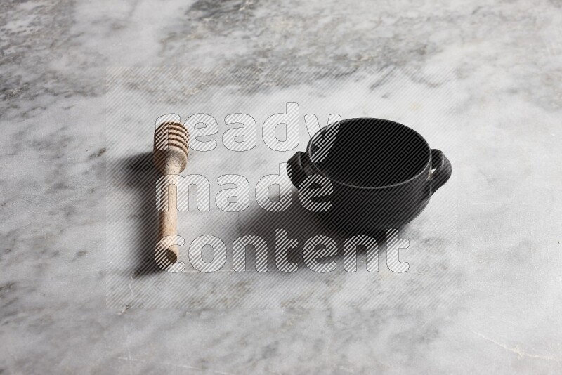 Black pottery bowl with wooden honey dipper on the side on grey marble background