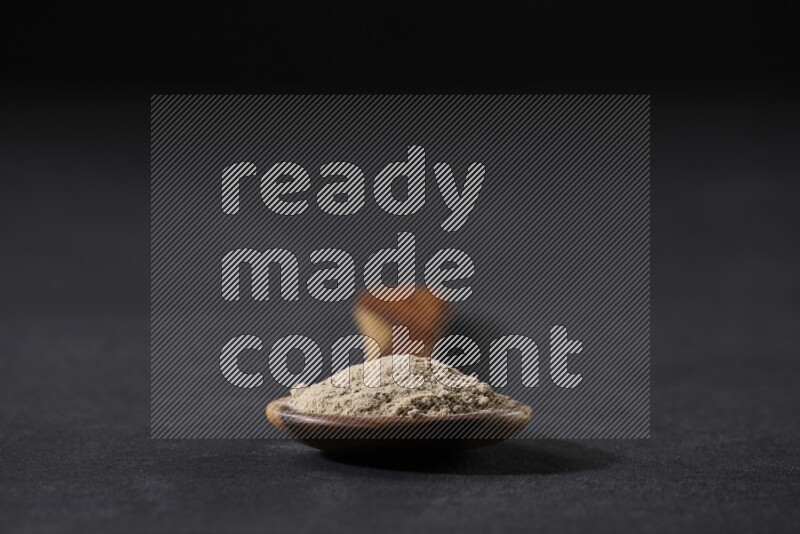 A wooden ladle full of garlic powder on a black flooring