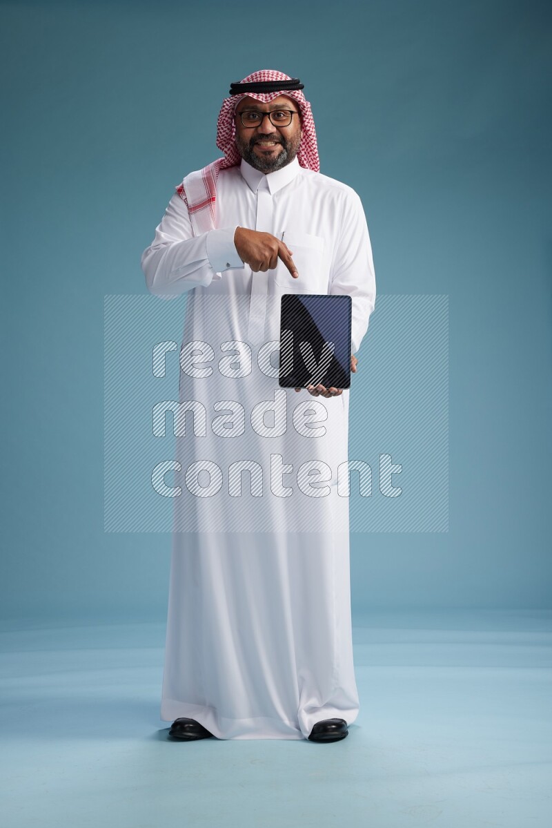 Saudi Man with shimag Standing holding a tablet on blue background