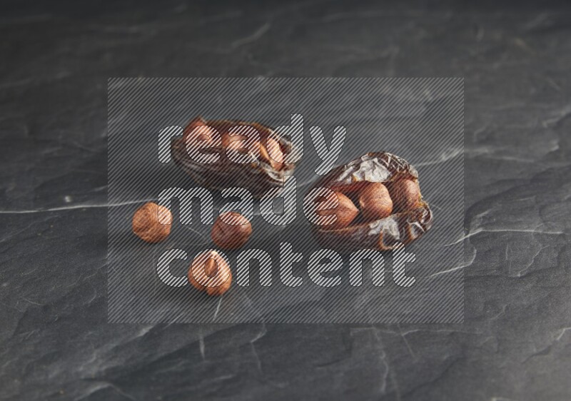 two hazelnuts stuffed madjoul dates on a black textured background