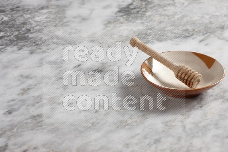Multicolored pottery plate with wooden honey dipper in it on grey marble background