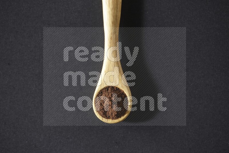 A wooden spoon full of cloves powder on a black flooring