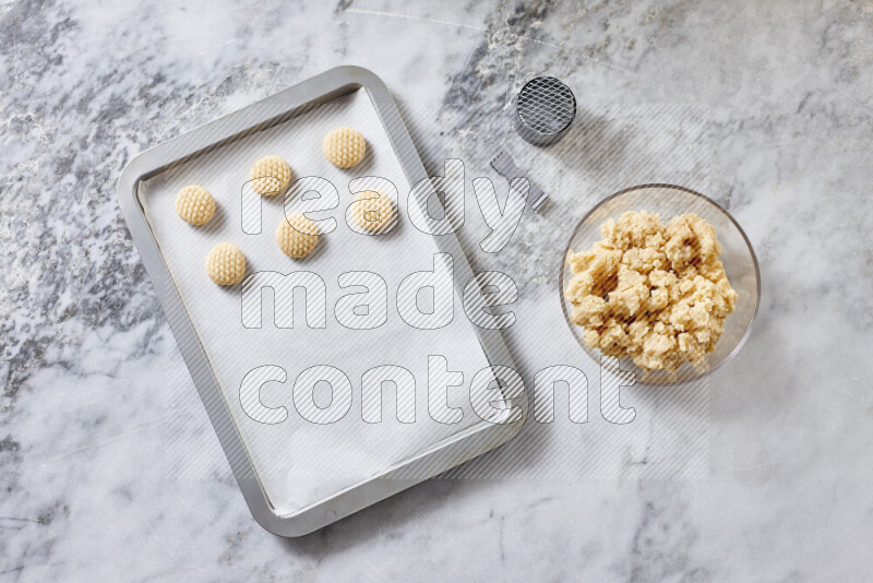 كحك خطوة بخطوة بمكوناته سمن، سكر، دقيق، سمسم، خميرة، ماء ونكهة الكحك على خلفية رخام رمادي