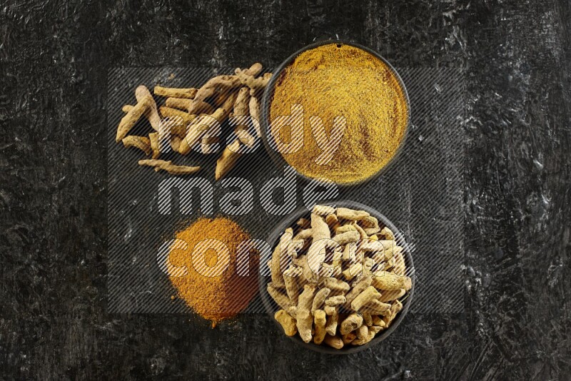 2 pottery black bowls, one full of turmeric powder and the other full of dried turmeric whole fingers on a textured black flooring