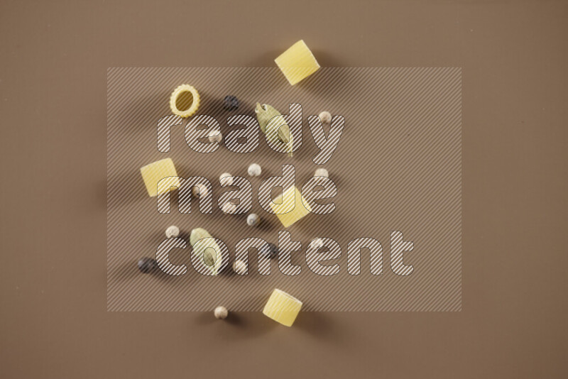 Raw pasta with different ingredients such as cherry tomatoes, garlic, onions, red chilis, black pepper, white pepper, bay laurel leaves, rosemary and cardamom on beige background