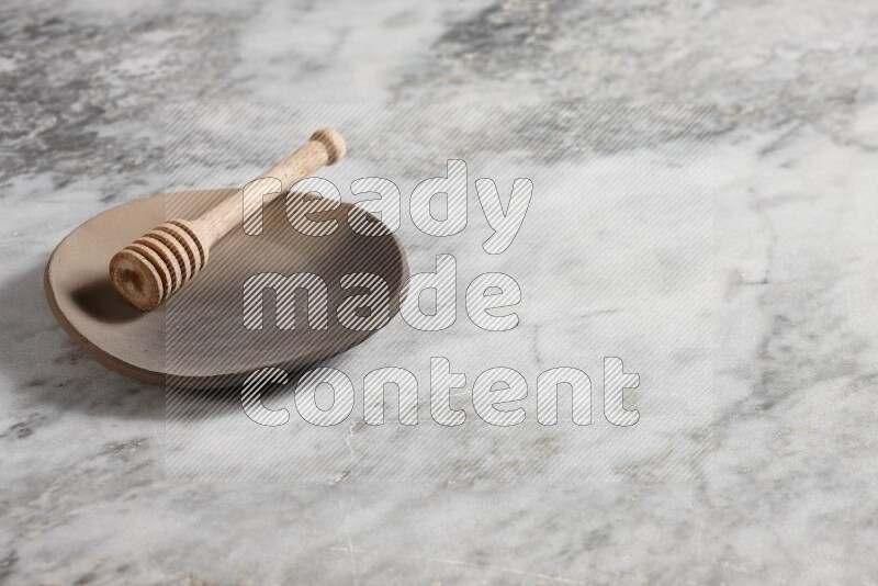 طبق فخاري متعدد الألوان مع ملعقة عسل خشبية بداخله على خلفية من الرخام الرمادي