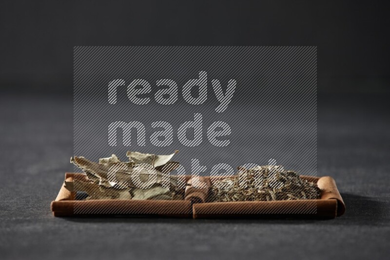 مربعان من أعواد القرفة ممتلئان بحبوب الكمون وأوراق الغار علي خلفية سوداء