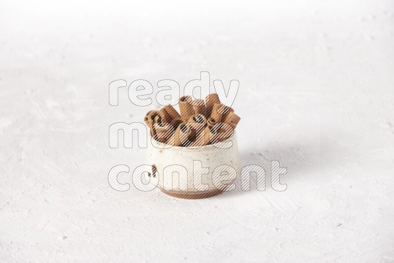 Cinnamon sticks in a beige bowl on a white background