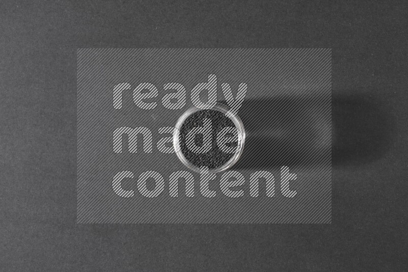 A glass jar full of black seeds on a black flooring