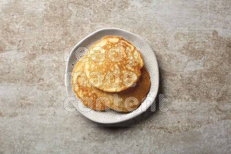Three stacked plain pancakes in an irregular plate on beige background