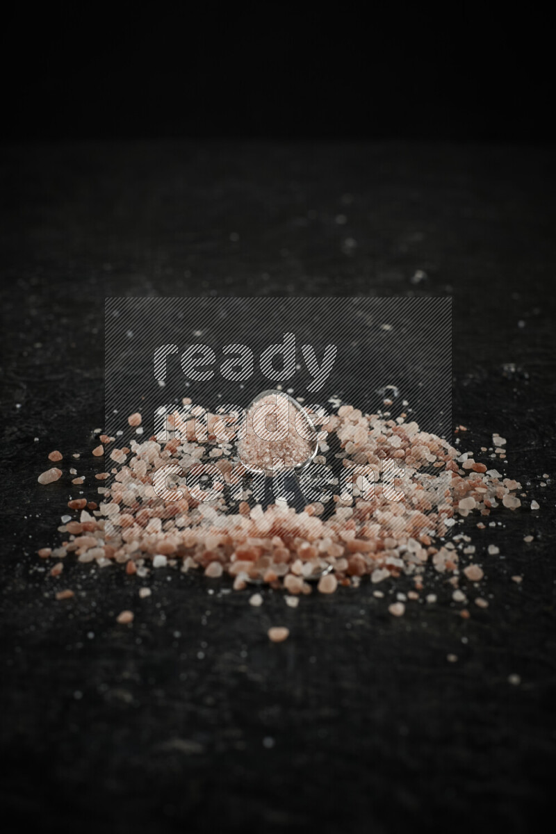 2 metal spoons filled with pink himalayan salt on black background