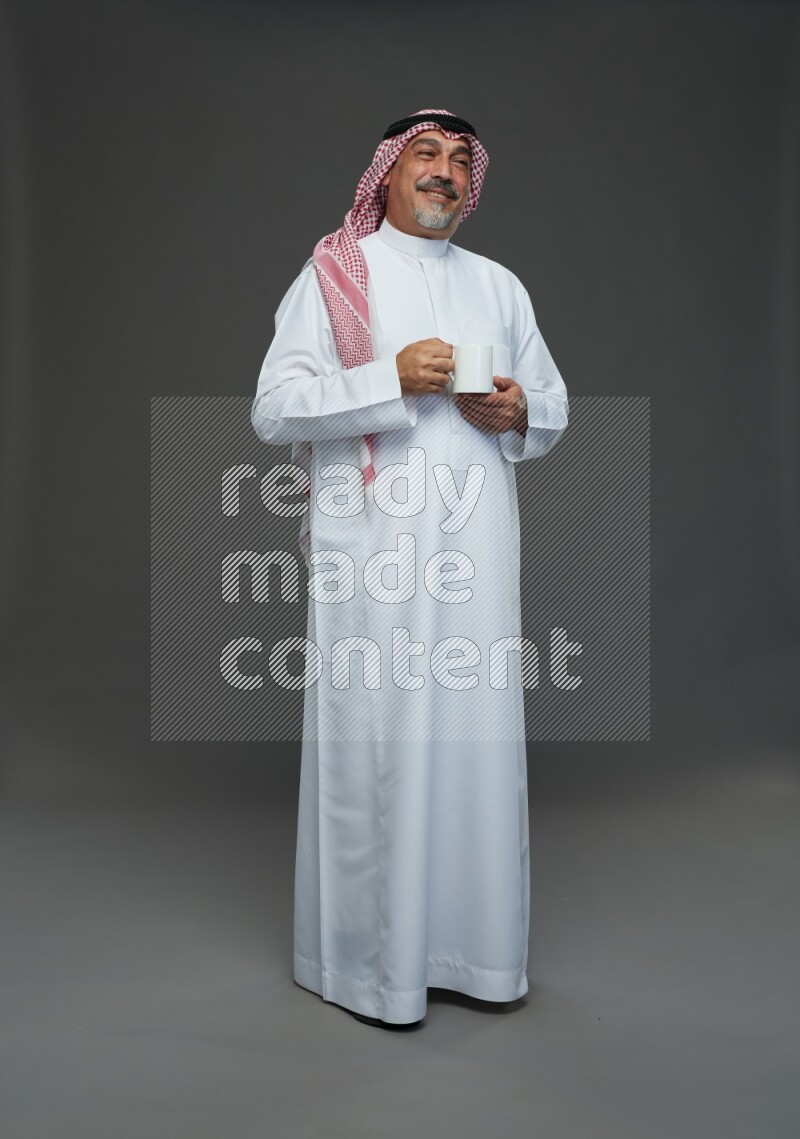 Saudi man with shomag Standing holding mug on gray background