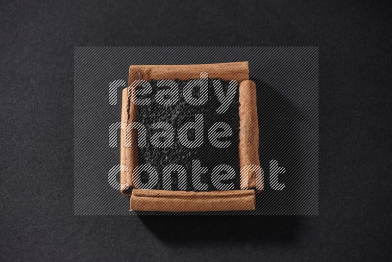 A single square of cinnamon sticks full of black seeds on black flooring