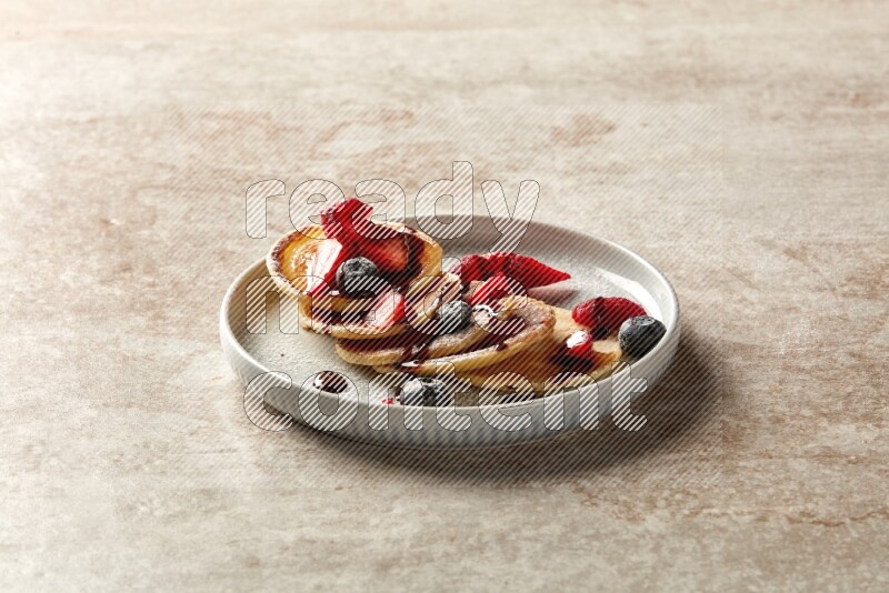 Five stacked mixed berries mini pancakes in a blue plate on beige background