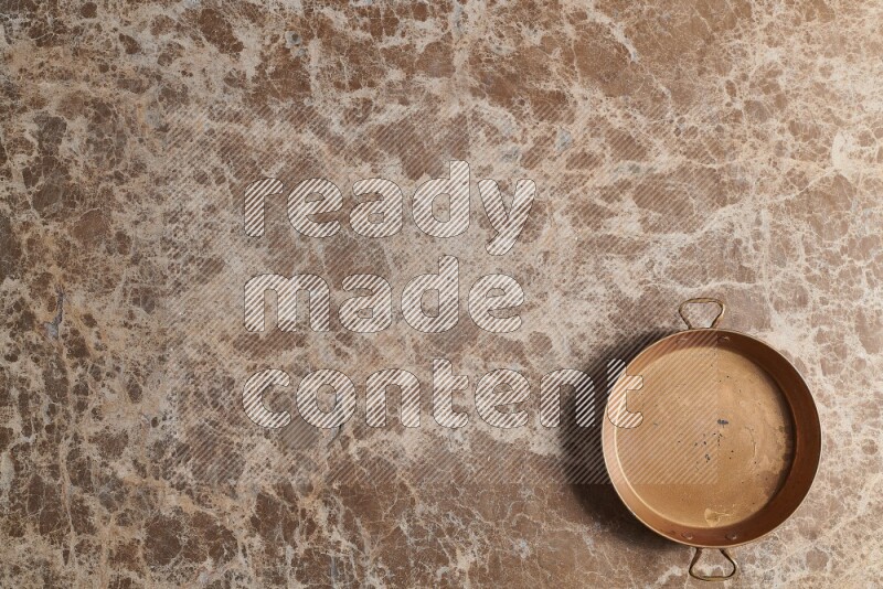 A small copper pan on beige marble background