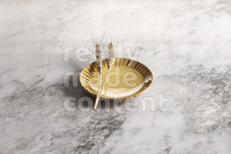 Wheat stalks on multicolored pottery plate on grey marble background