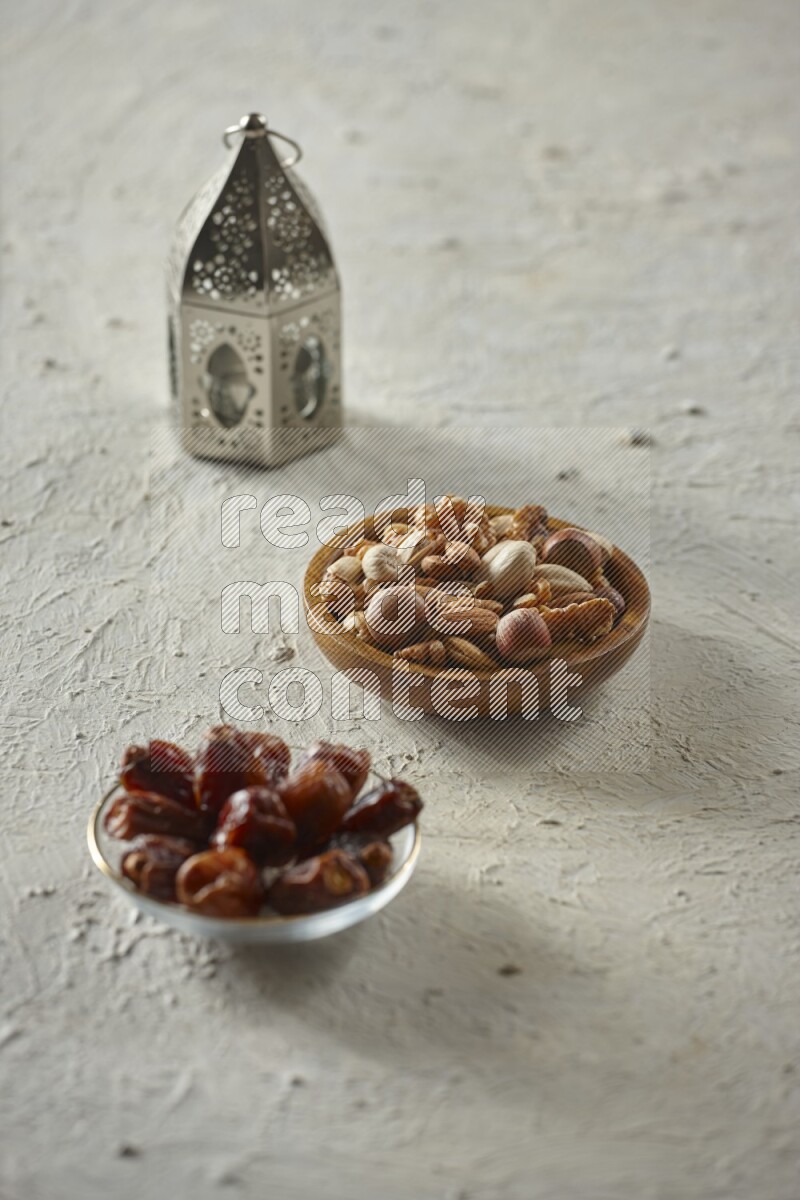 A silver lantern with different drinks, dates, nuts, prayer beads and quran on textured white background