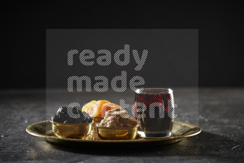 Dried fruits in metal bowls with tamarind on a tray in dark setup