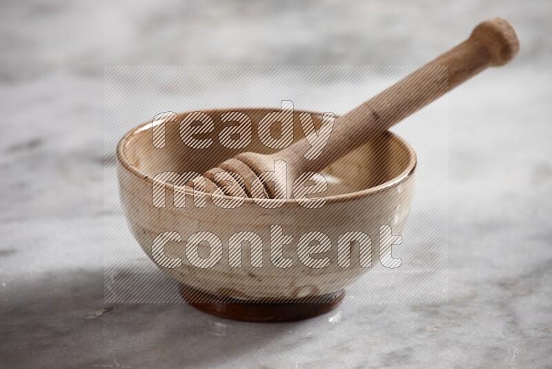 Beige pottery bowl with wooden honey dipper in it on grey marble background