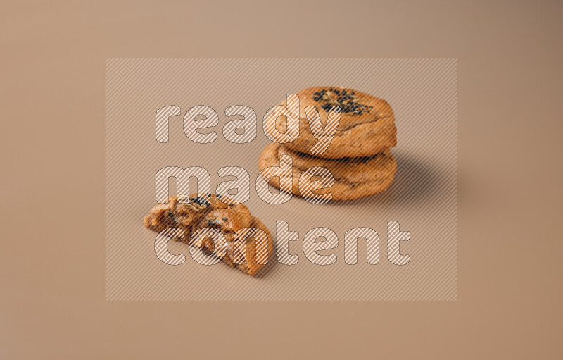 Two Hasawi cookies field of date and decorated by black seed and anise grain with another one cut in half on a brown background