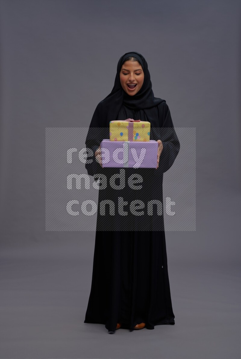 Saudi woman wearing Abaya standing holding gift box on gray background