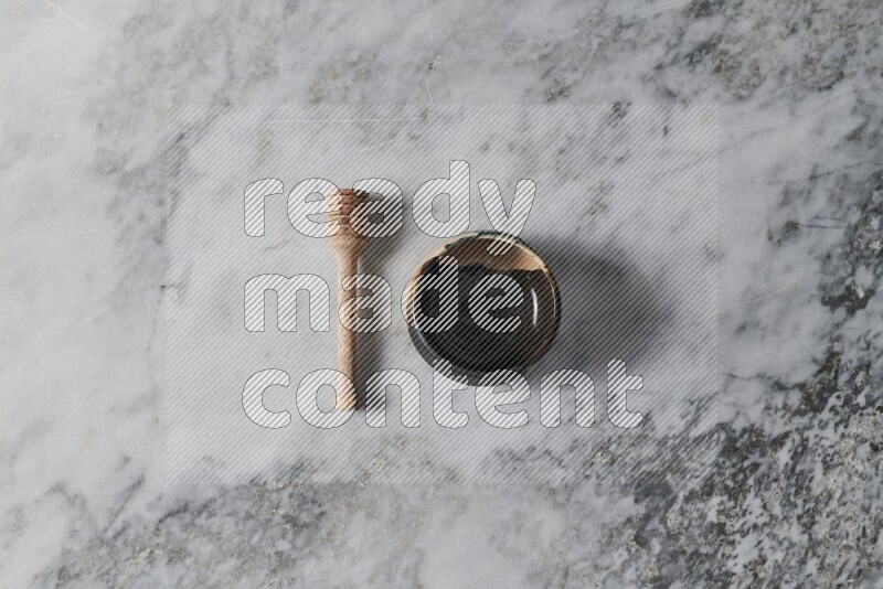 Multicolored pottery bowl with wooden honey dipper on the side on grey marble background