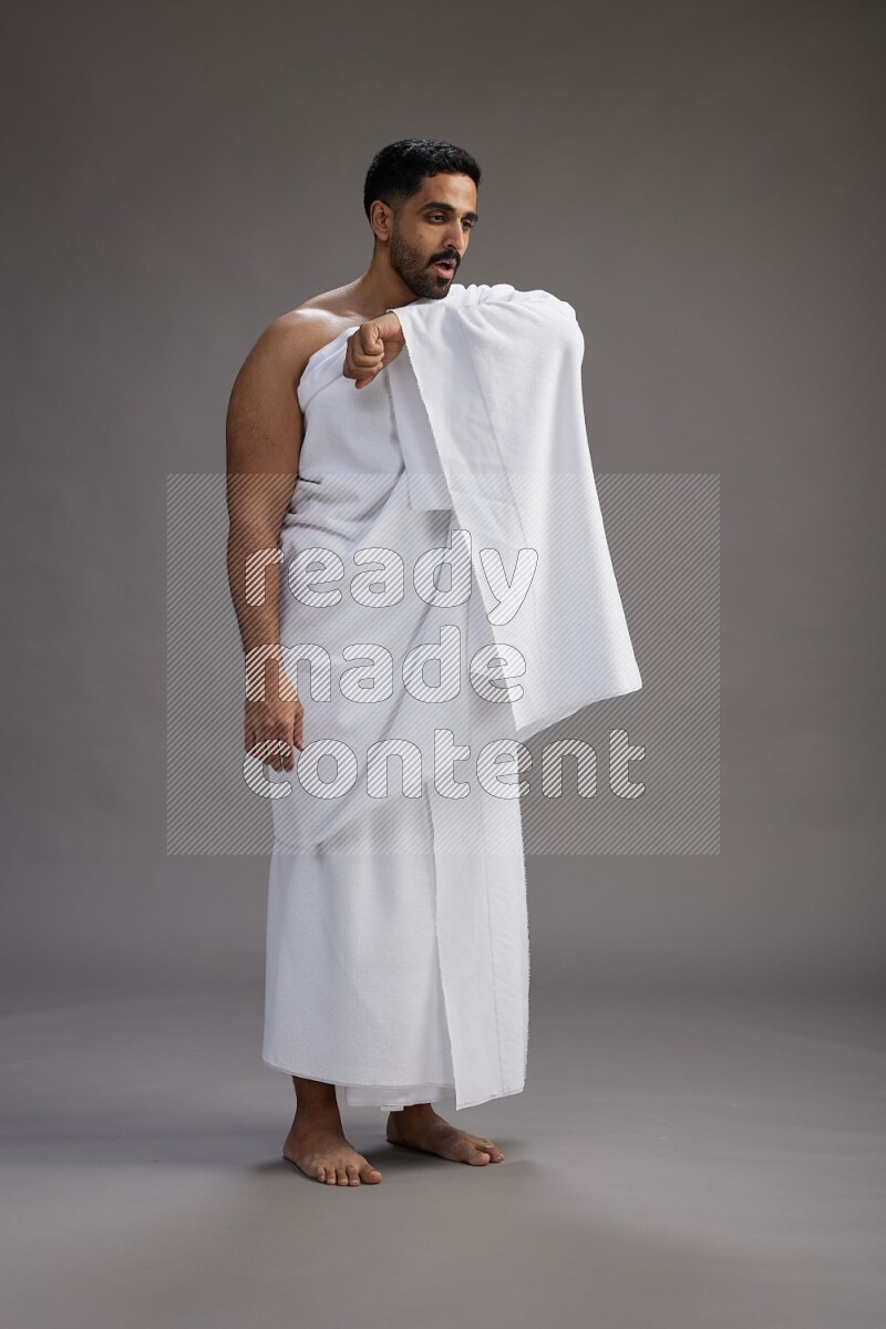 A man wearing Ehram standing showing how to sneeze on gray background