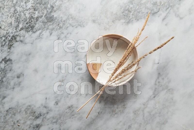 Wheat stalks on multicolored pottery plate on grey marble background