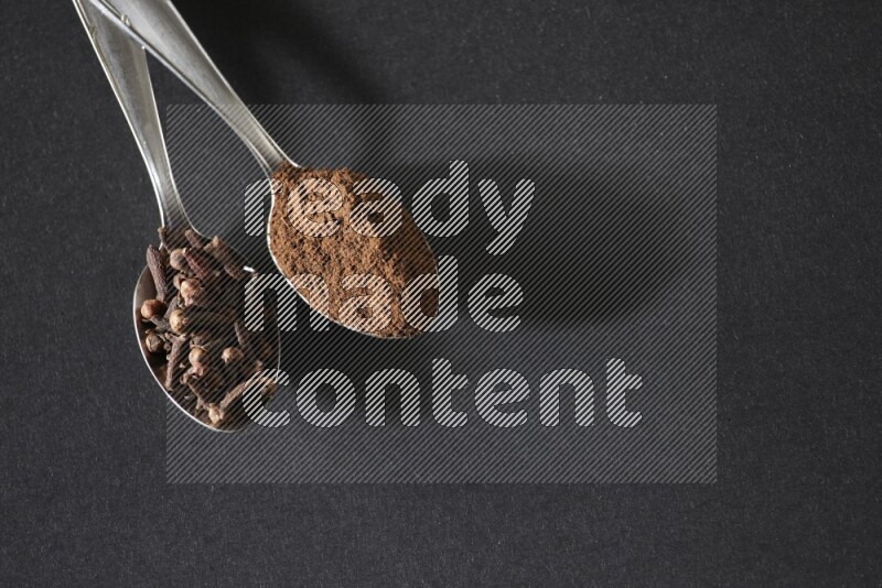 ملعقتان معدنيتان، إحداهما ممتلئة بحبوب القرنفل والأخرى ببودرة القرنفل، على خلفية سوداء