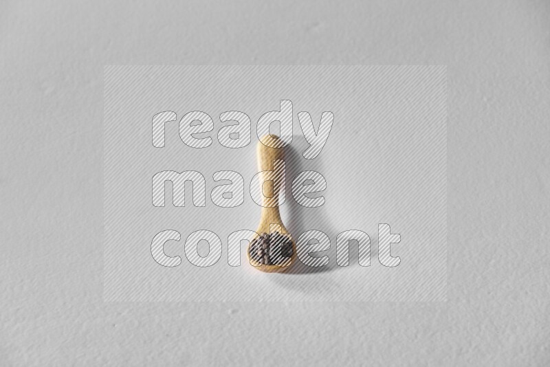 A wooden spoon full of black pepper on white flooring