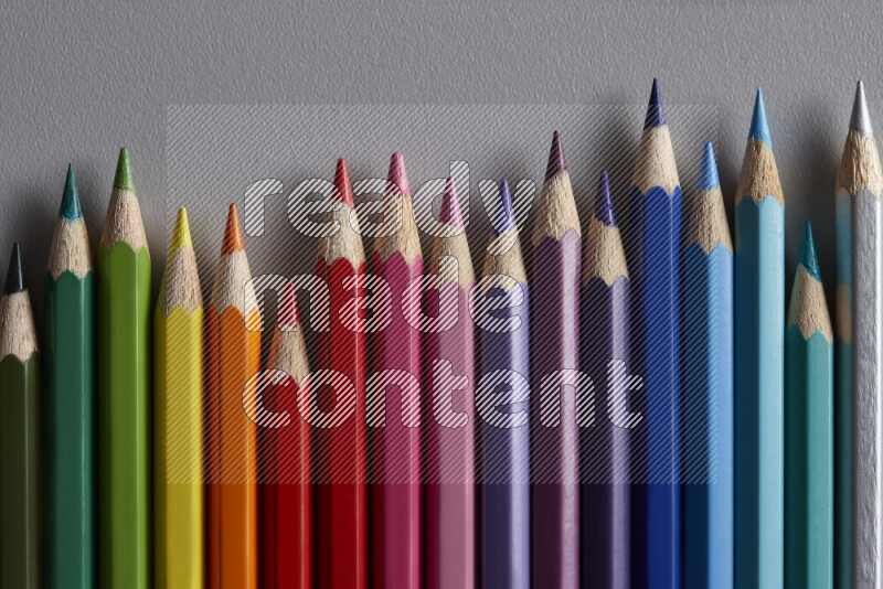 A collection of colored pencils arranged showcasing a gradient of different hues on grey background