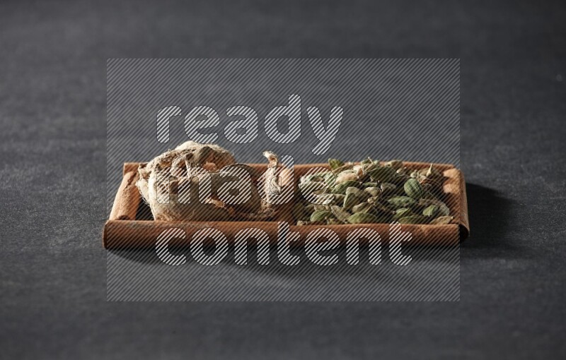 مربعان من أعواد القرفة ممتلئان بحبوب الهيل والزنجبيل المجفف علي خلفية سوداء