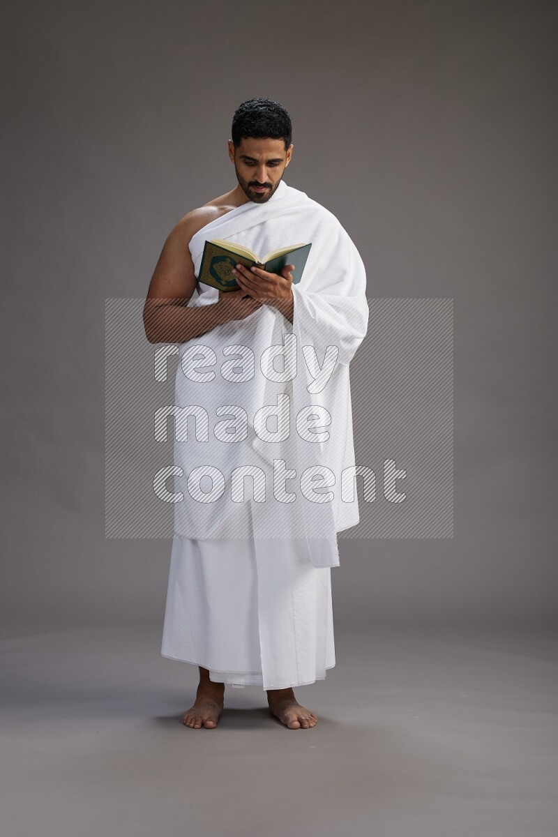 A man wearing Ehram Standing reading quran on gray background