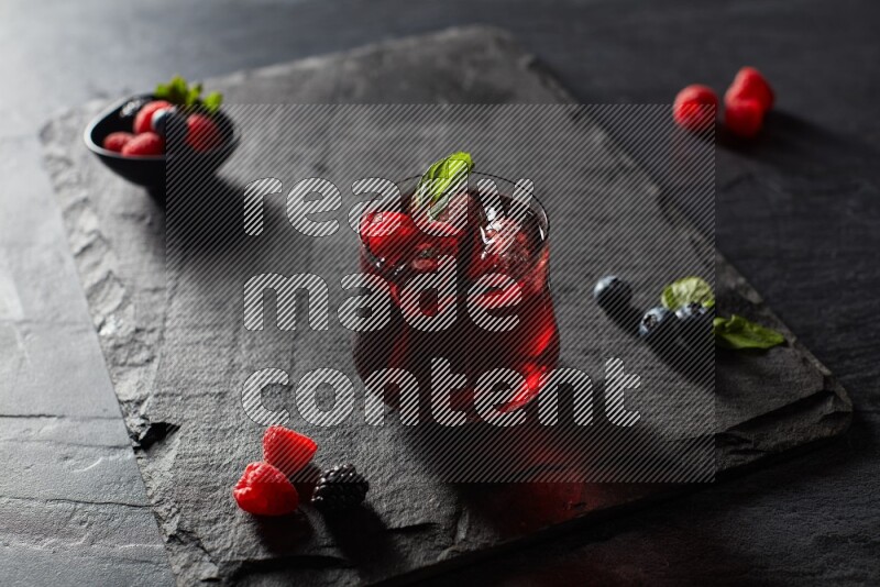 A glass of mixed berries juice with mint leaves on black background