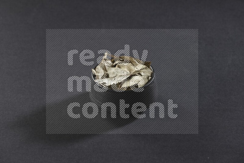 وعاء فخاري أسود ممتلئ بأوراق الغار المجففة على أرضية سوداء